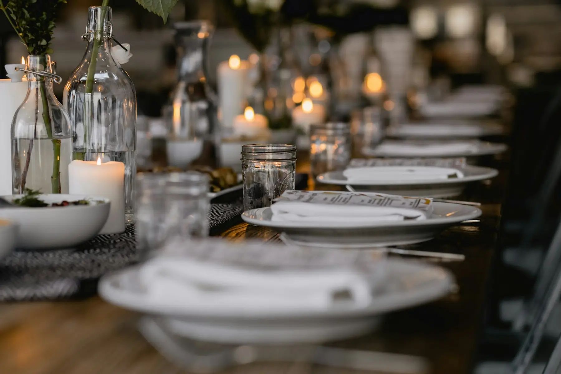 Long dinner table set with white plates and glowing candles