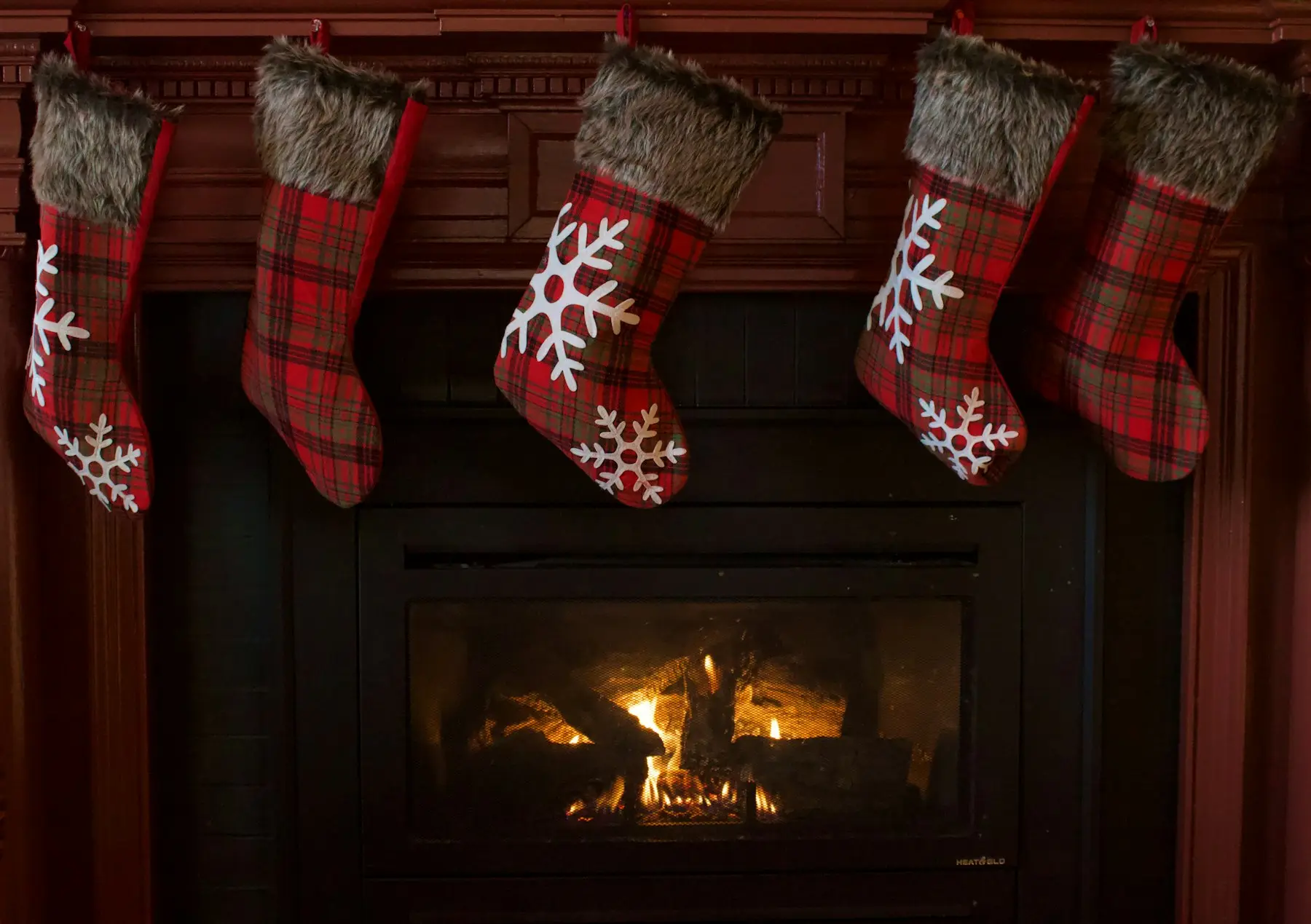 Red and white knit stockings hanging over a lit fireplace